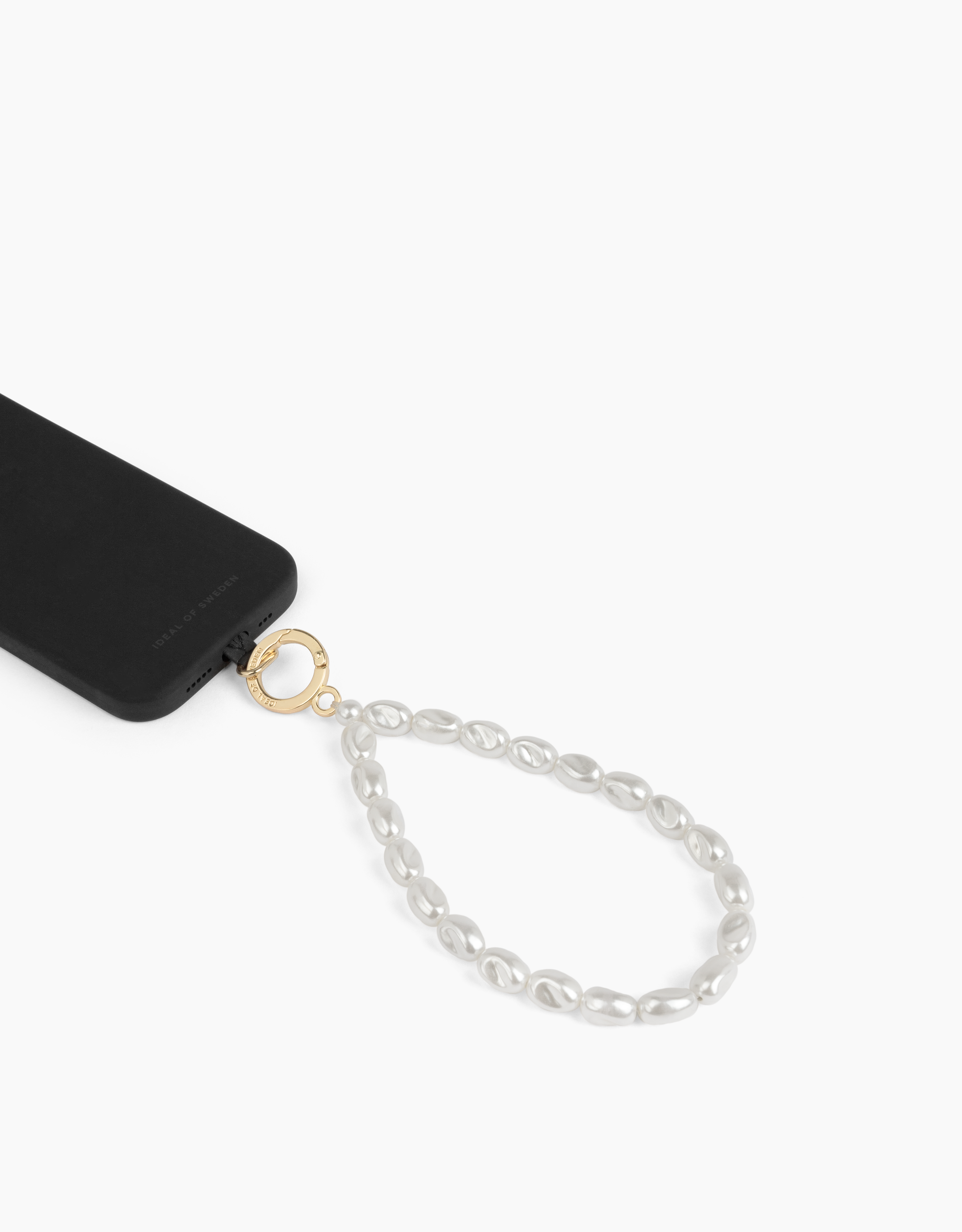 Schwarzes Telefon mit Perlenband. Das Telefon ist mit einem goldenen Ring mit weißen Perlen auf weißem Hintergrund verbunden.