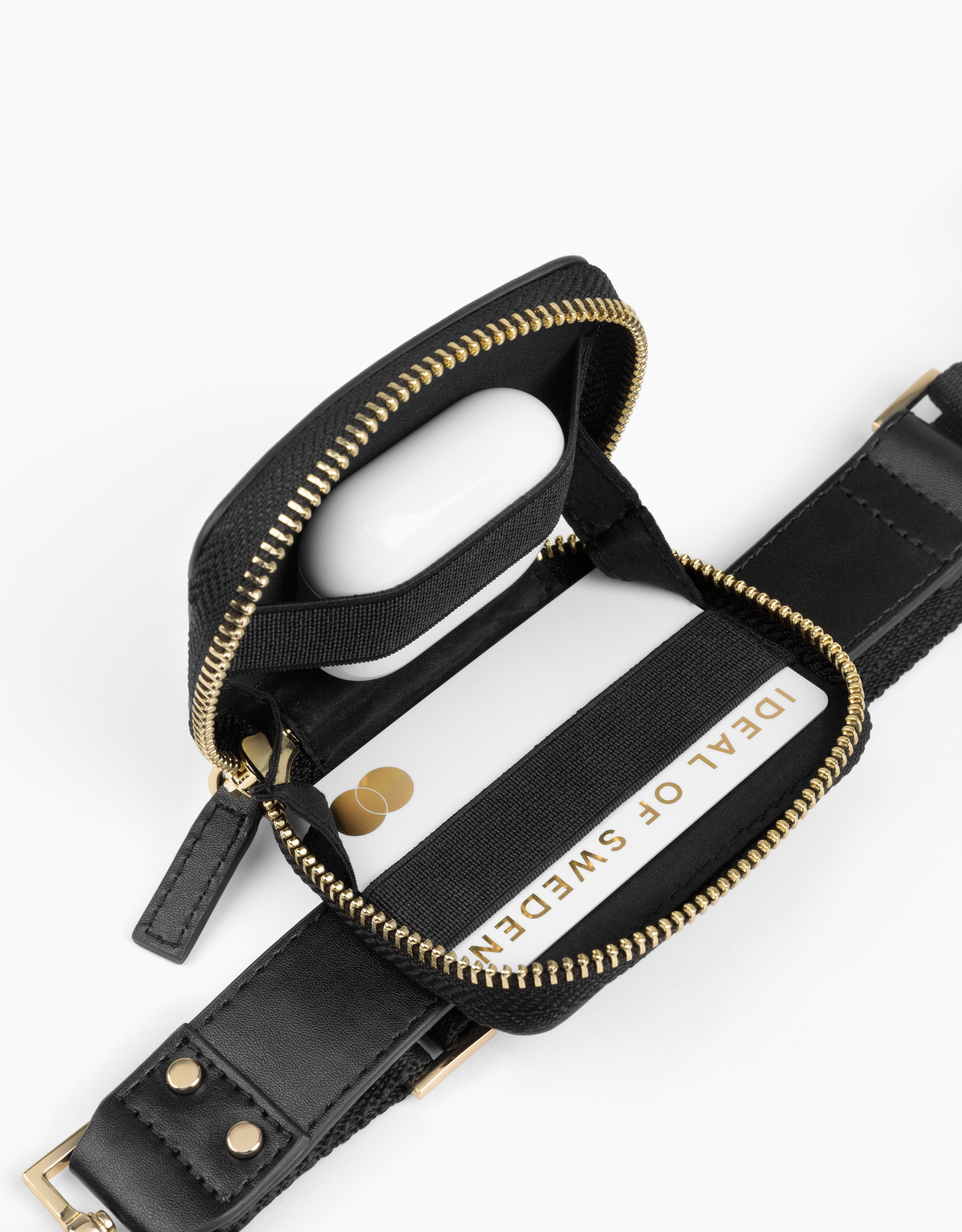 Schwarze Reißverschlusstasche mit goldenem Reißverschluss, mit weißen Ohrhörern und einer Karte mit IDEAL OF SWEDEN.