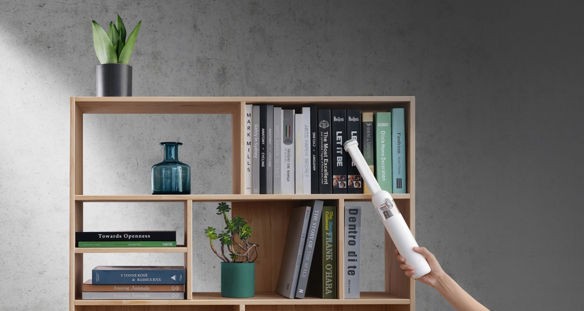 Drewniany regał z książkami, roślinami i odkurzaczem czyszczącym go. Szare tło.