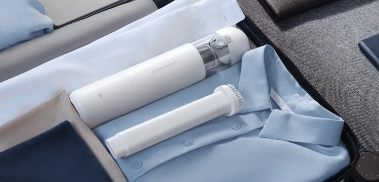 Otwarta walizka ze złożonymi koszulami i białym odkurzaczem i szczotką w środku. Widoczne są inne elementy garderoby.