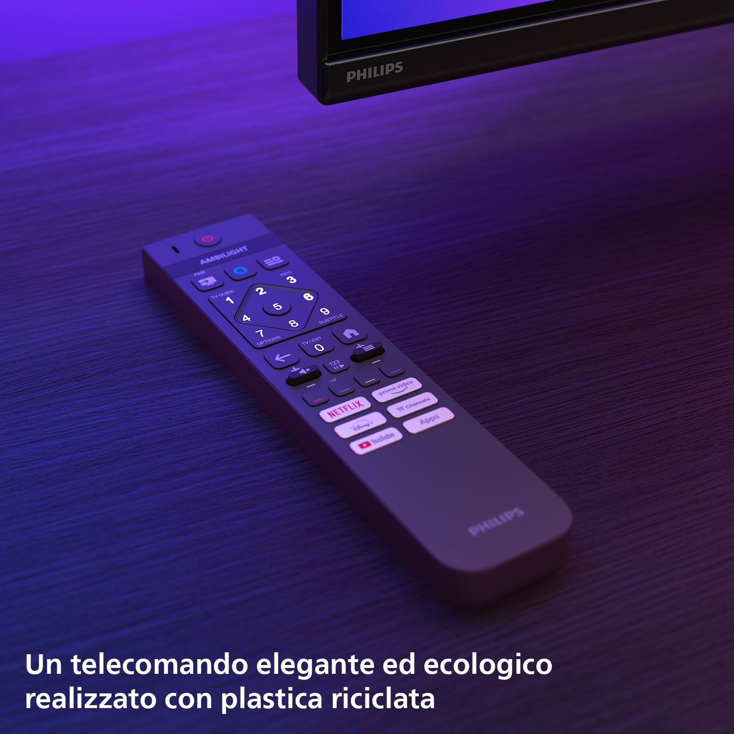 Un telecomando Philips su un tavolo di legno. Il telecomando è grigio scuro con pulsanti bianchi. Una TV sullo sfondo.