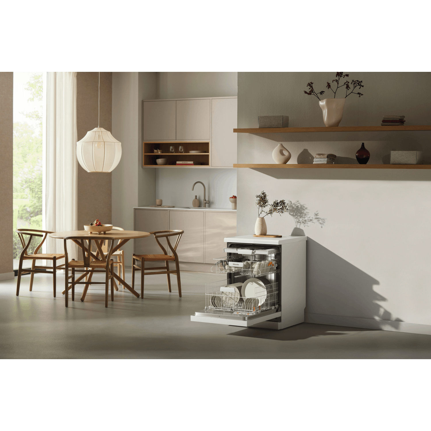 A modern kitchen with a dishwasher, dining table, and chairs. The dishwasher is open, and the table has fruit.