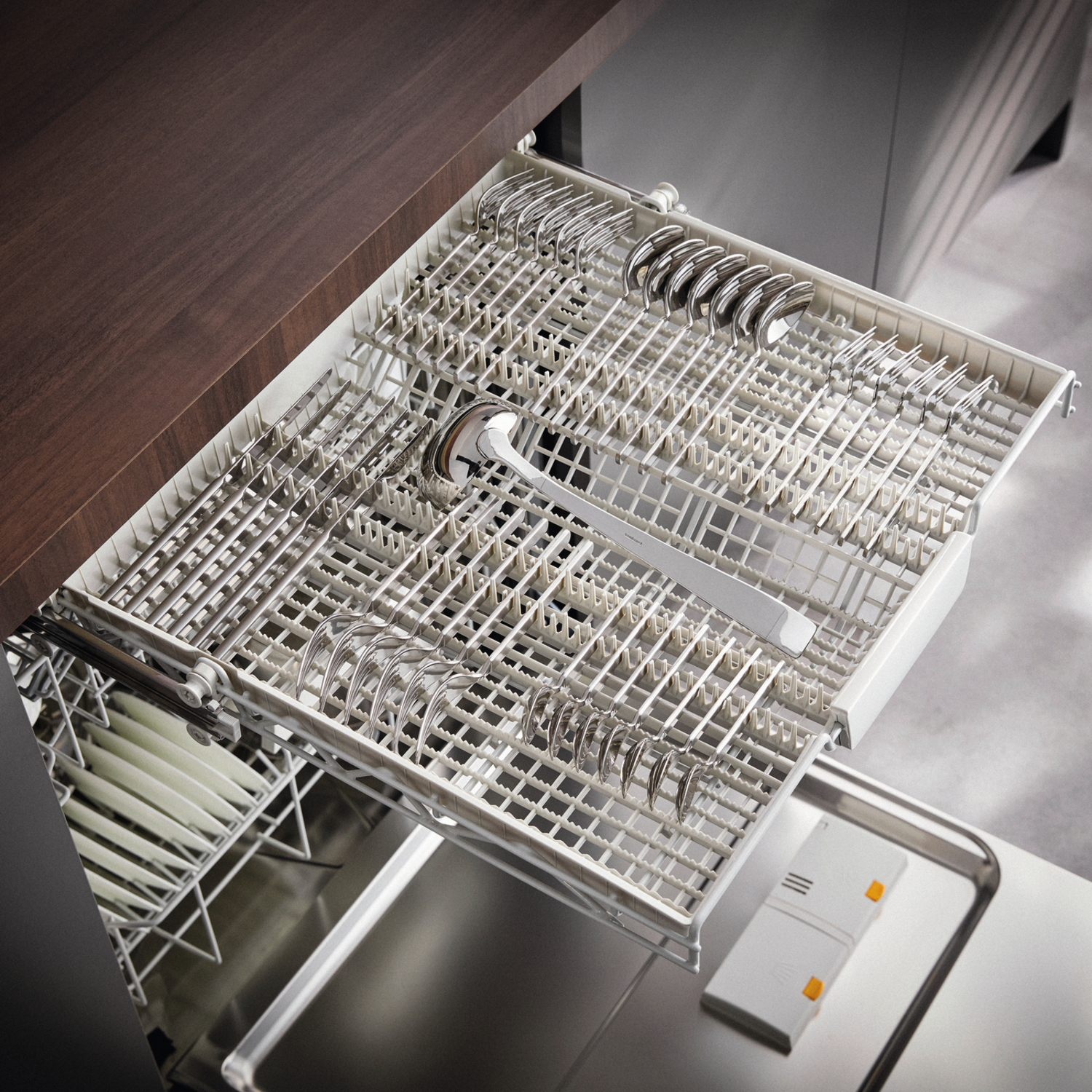 Open dishwasher drawer with silverware and dishes. Spoons, forks, and knives are organized. The drawer is partially open.