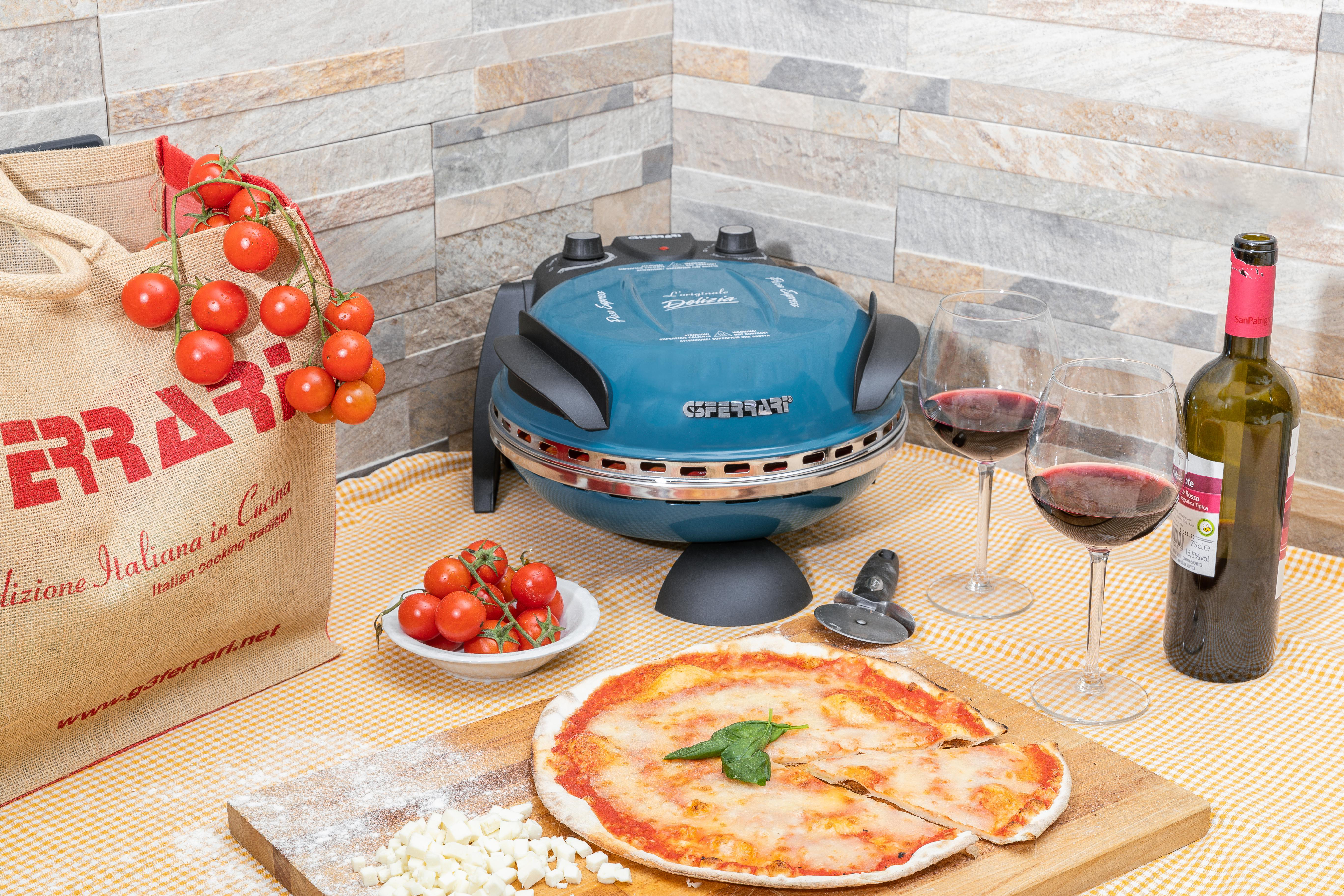 Eine Pizza mit Tomaten, Mozzarella und Basilikum befindet sich in der Nähe eines Pizzaofens, Weingläsern und einer Weinflasche. Eine Tüte Tomaten steht daneben.