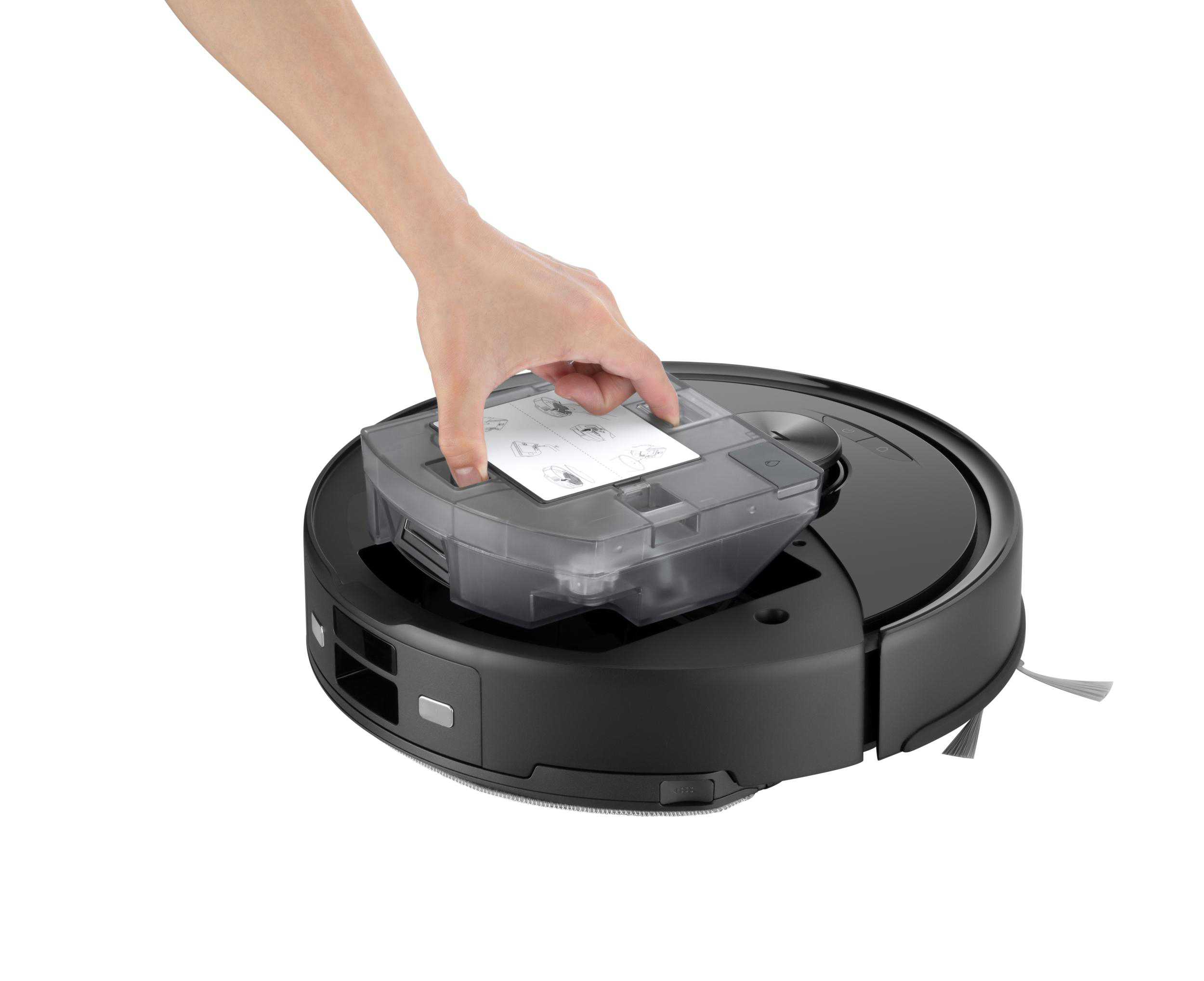 Eine Hand setzt einen transparenten Behälter in einen schwarzen Roboter-Staubsauger. Der Staubsauger steht auf weißem Untergrund.