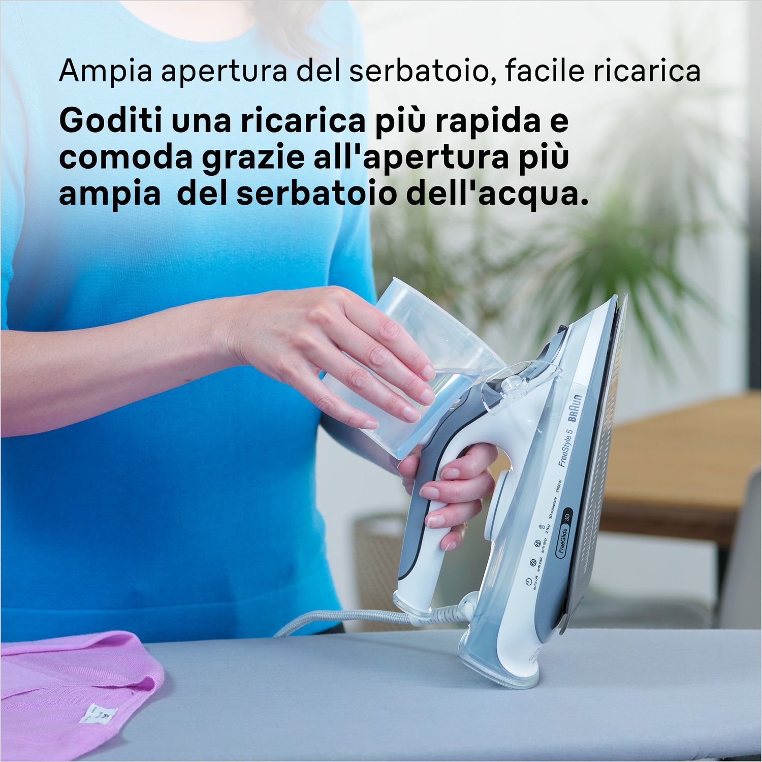 Una donna riempie un ferro da stiro bianco e grigio con acqua da un contenitore. Il ferro è su un asse da stiro grigio vicino a una camicia rosa.