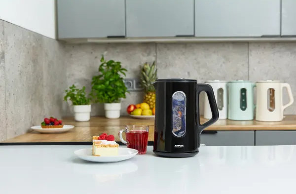 Scena kuchenna z czarnym czajnikiem, ciastem i herbatą. W tle inne czajniki i rośliny.