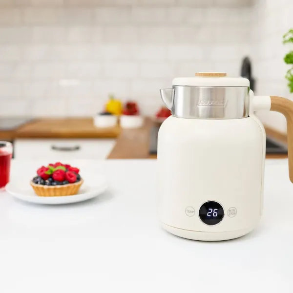 Biały czajnik z drewnianym uchwytem stoi na blacie. Obok tarty z jagodami i szklanka soku.