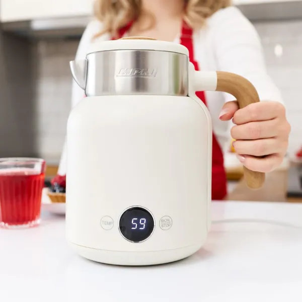 Kobieta trzyma biały czajnik elektryczny z drewnianym uchwytem. W pobliżu szklanka czerwonego płynu i tarty. Wyświetlacz pokazuje 59.