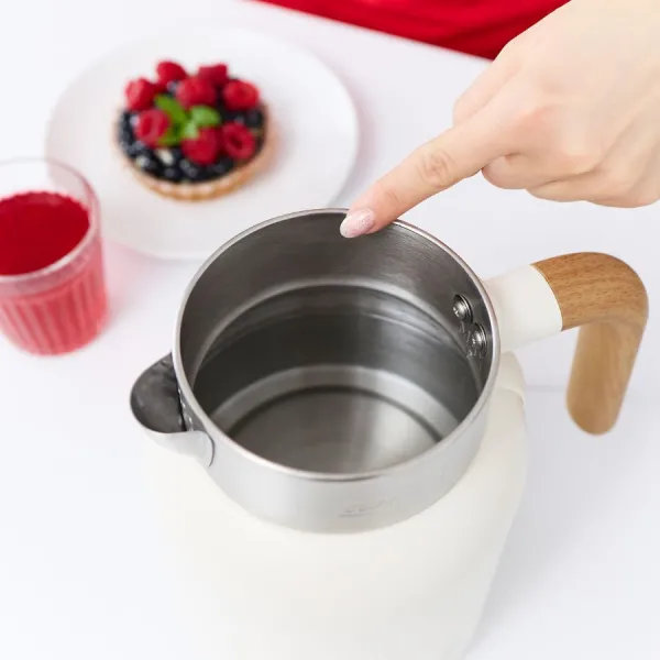 Palec wskazuje na srebrny czajnik. Na stole znajduje się również talerz z tartą jagodową i szklanka soku.