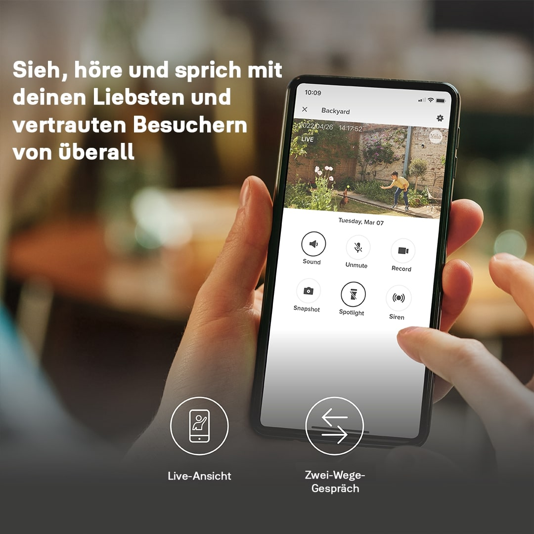 Eine Hand hält ein Telefon, das eine Kameraansicht des Hinterhofs zeigt. Optionen sind Ton, Stummschaltung aufheben, aufnehmen, Schnappschuss, Scheinwerfer und Sirene.