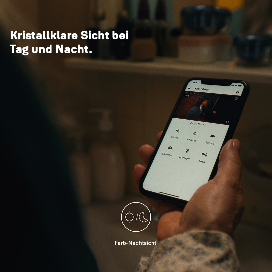 Eine Hand hält ein Smartphone mit Live-Video. Der Bildschirm zeigt eine Person und Steuerungstasten für Ton, Stummschaltung und Aufnahme.