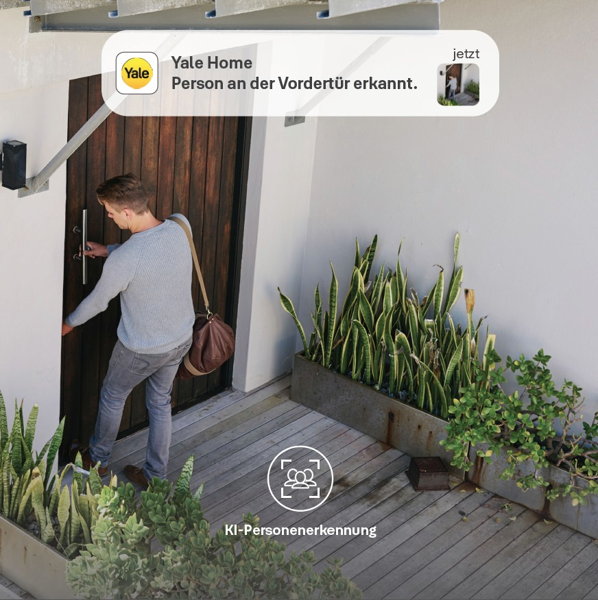 Ein Mann öffnet eine Holztür. Eine Yale Home-Benachrichtigung besagt, dass eine Person an der Haustür erkannt wurde. Pflanzen sind im Vordergrund.