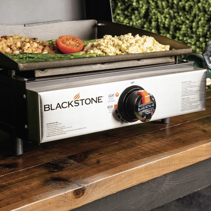 Grill Blackstone z jedzeniem. Zawiera pomidory, jajecznicę, szparagi i hash browns. Grill stoi na drewnianej powierzchni.