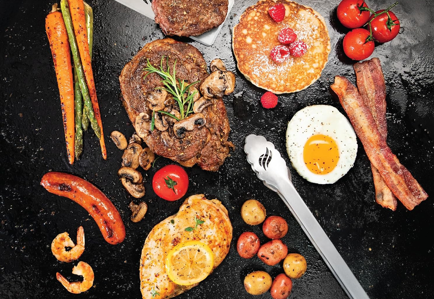 Widok z góry na różne gotowane potrawy: stek, naleśniki, bekon, jajka, warzywa, kiełbasa, krewetki, kurczak, ziemniaki i pomidory.