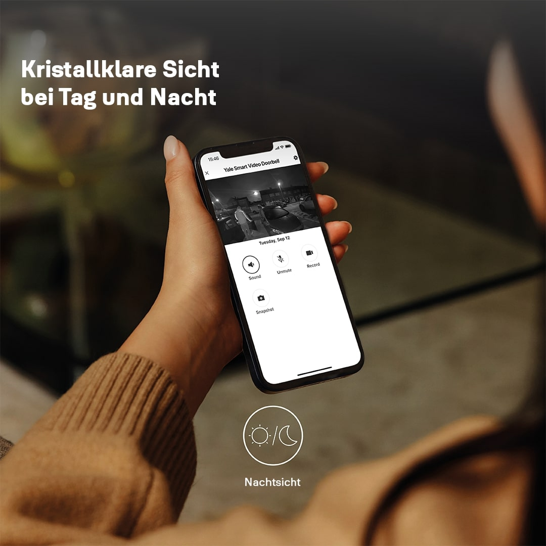 Eine Hand hält ein Telefon, das eine Nachtsichtansicht einer Überwachungskamera zeigt. Text: 'Kristallklare Sicht bei Tag und Nacht'.