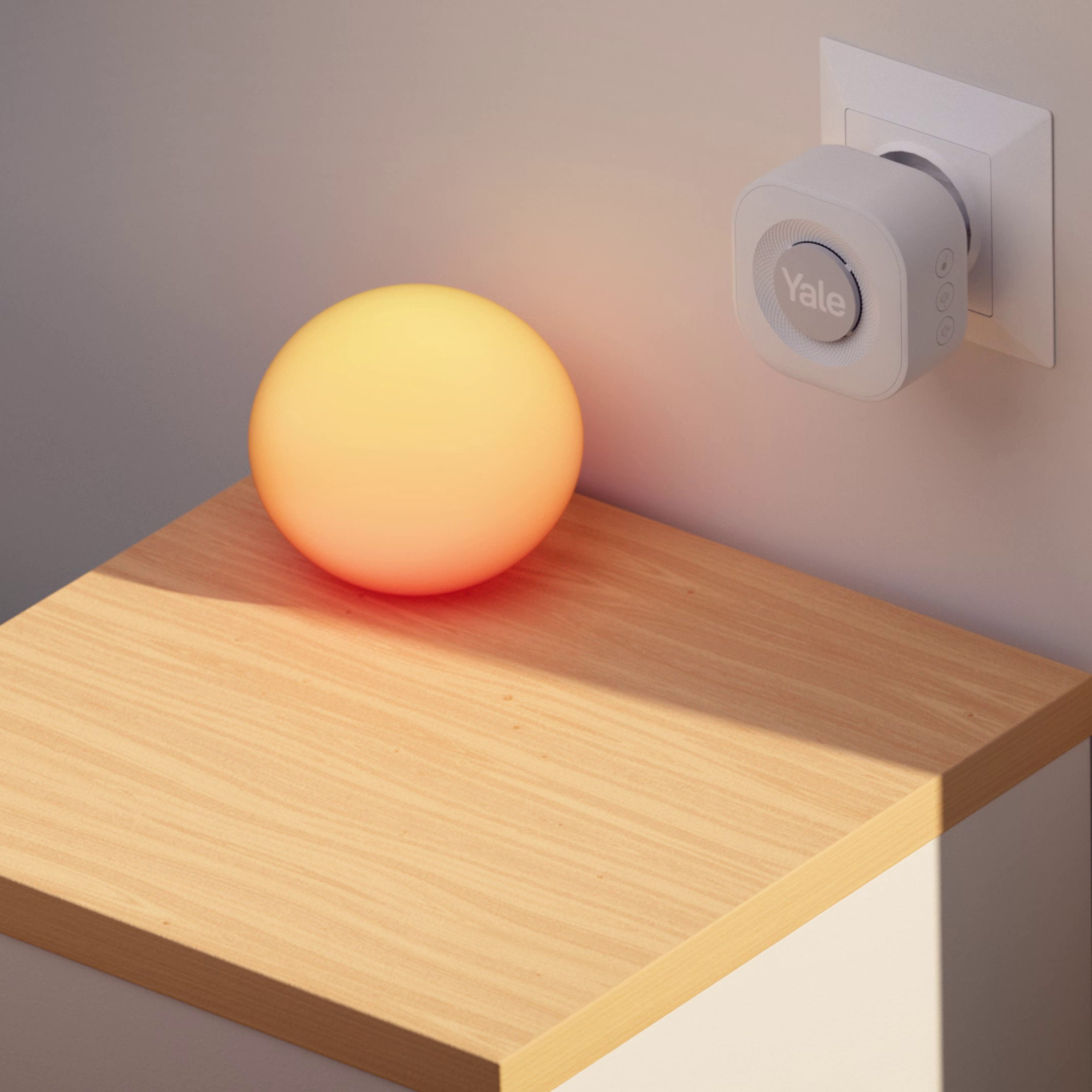 Eine leuchtende orangefarbene Kugel auf einem Holztisch, ein Yale-Gerät an der Wand.