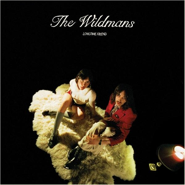 Albumcover. Zwei Personen sitzen auf einem flauschigen Teppich vor einem schwarzen Hintergrund. Der Text „The Wildmans“ steht oben. Einer trägt Rot, der andere Weiß.