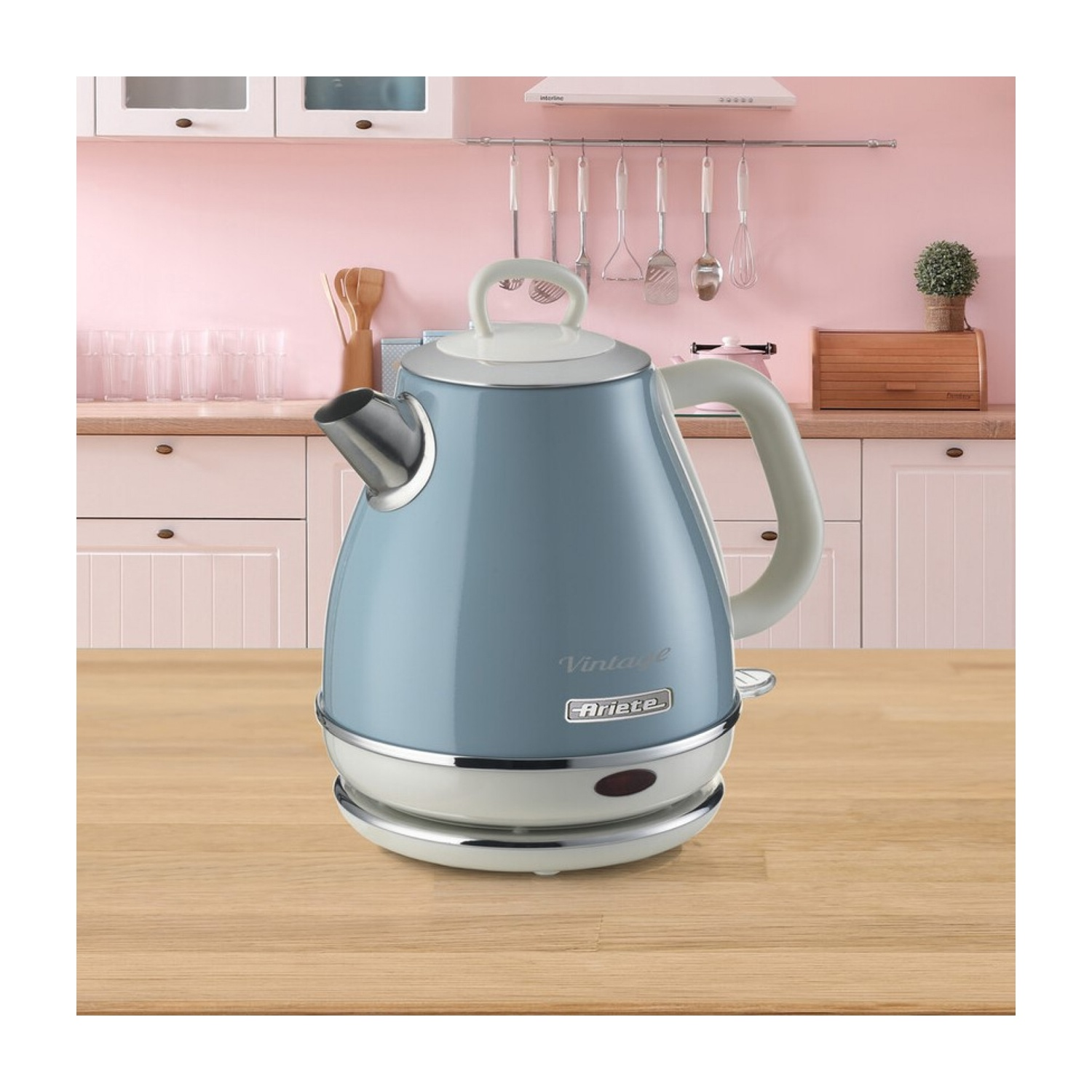 Un bollitore blu vintage su una superficie di legno. Ambiente cucina con parete rosa e armadi bianchi. Utensili appesi sullo sfondo.