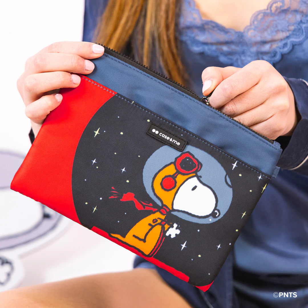 Kobieta trzyma etui z Snoopy'm w skafandrze kosmicznym. Etui jest czarne, czerwone i niebieskie. Gwiazdy i księżyc w tle.