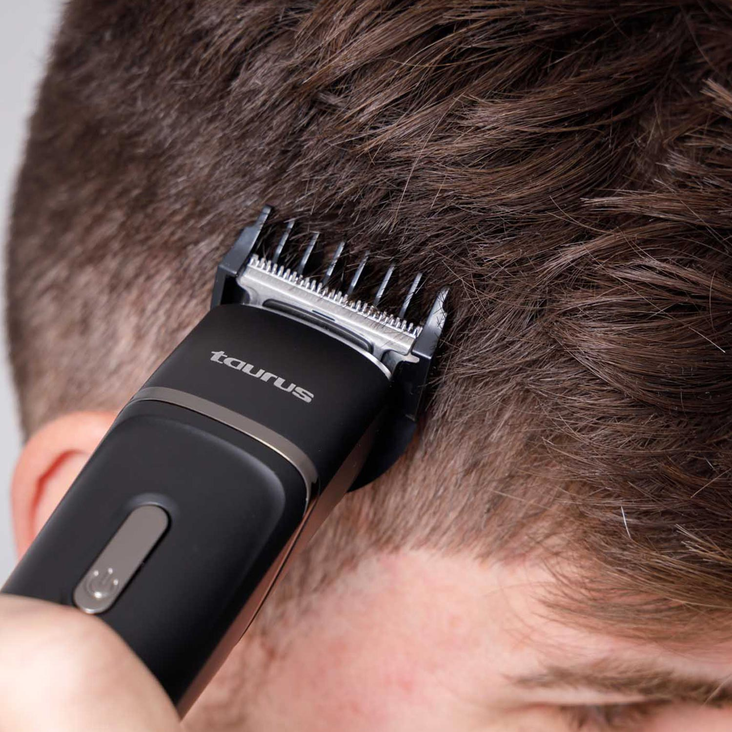 Una persona usa una cortadora de pelo Taurus negra para cortar cabello castaño. La cortadora está cerca de la cabeza.