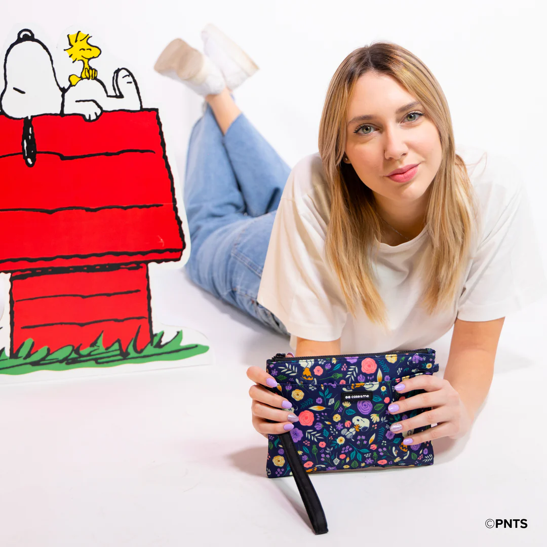 Kobieta leży na białej powierzchni, trzymając kwiatową kopertówkę. W pobliżu wycięcie domu Snoopy'ego oraz Snoopy i Woodstock.