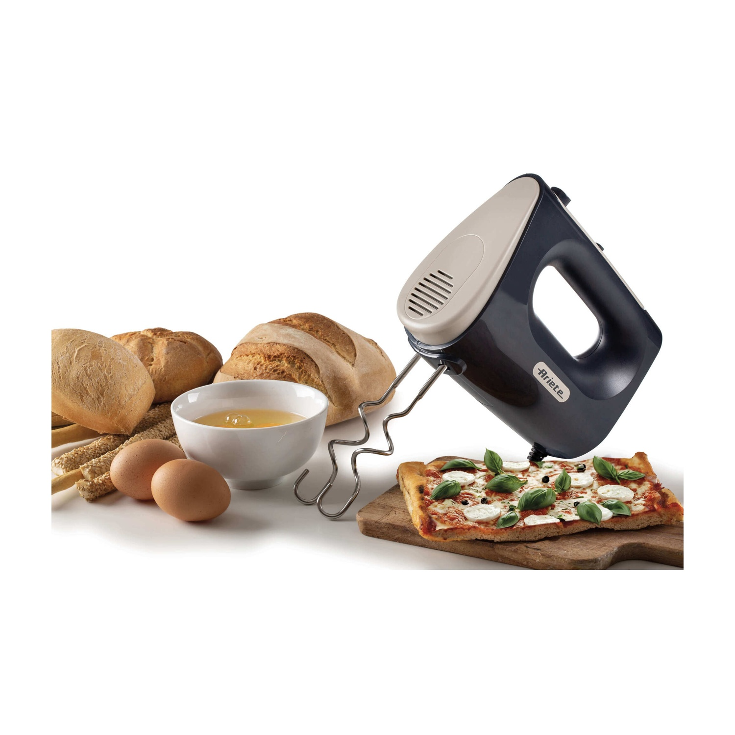 Un frullatore elettrico sopra una pizza su un tagliere, vicino a pane, uova e una ciotola di liquido. Sfondo bianco.