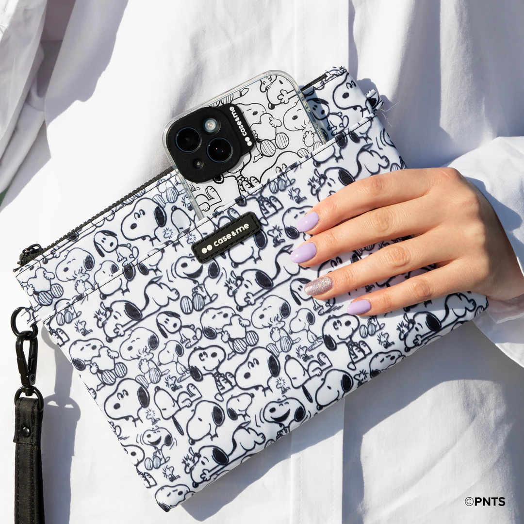 Dłoń trzyma torebkę ze wzorem Snoopy z telefonem. Etui na telefon również zawiera Snoopy'ego. Osoba ma na sobie białą koszulę i fioletowe paznokcie.