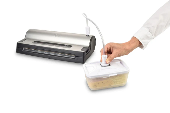 Zgrzewarka próżniowa z białą rurką połączoną z pojemnikiem trzymanym przez osobę. Pojemnik zawiera jedzenie.