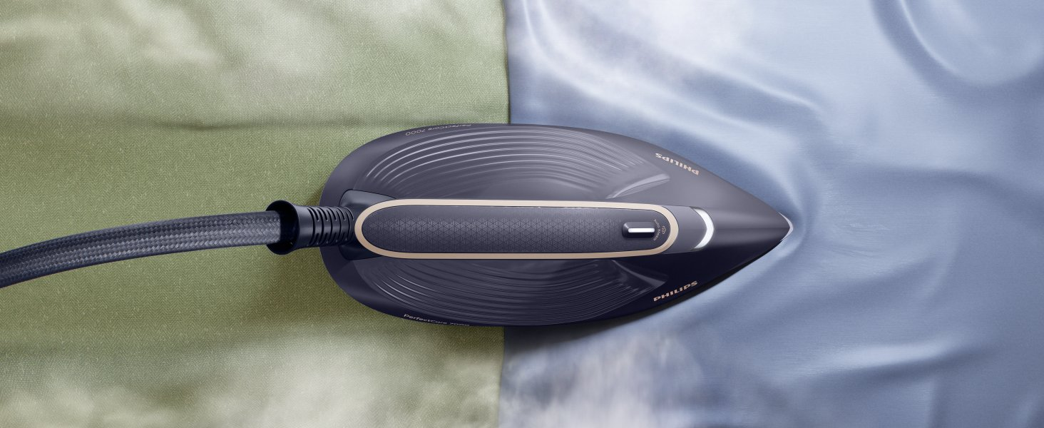 Una plancha azul oscuro con un acento dorado está sobre tela azul claro y verde. El cable es negro.
