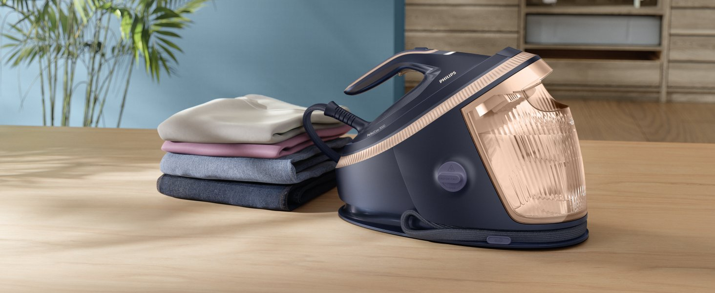Una plancha Philips azul oscuro con detalles en oro rosa junto a una pila de ropa doblada sobre madera.