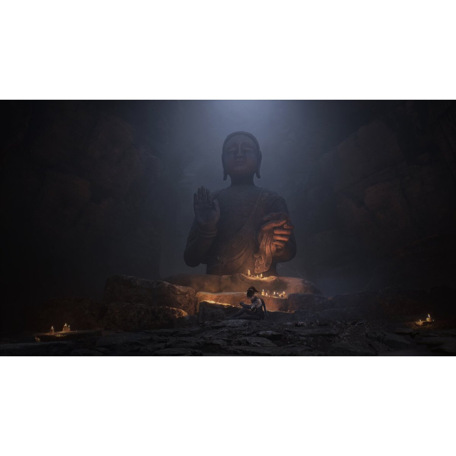 Une grande statue de Bouddha dans une grotte, des bougies allumées devant. Une personne médite devant la statue.