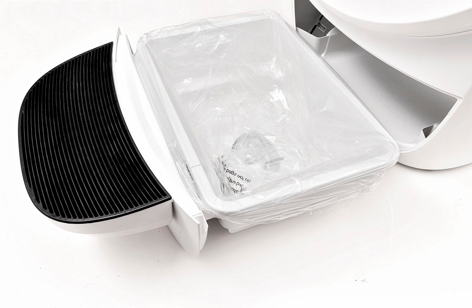 Weißer Katzenstreu-Kasten mit klarer Plastiktüte. Schwarze Gitter links. Die Box ist offen.