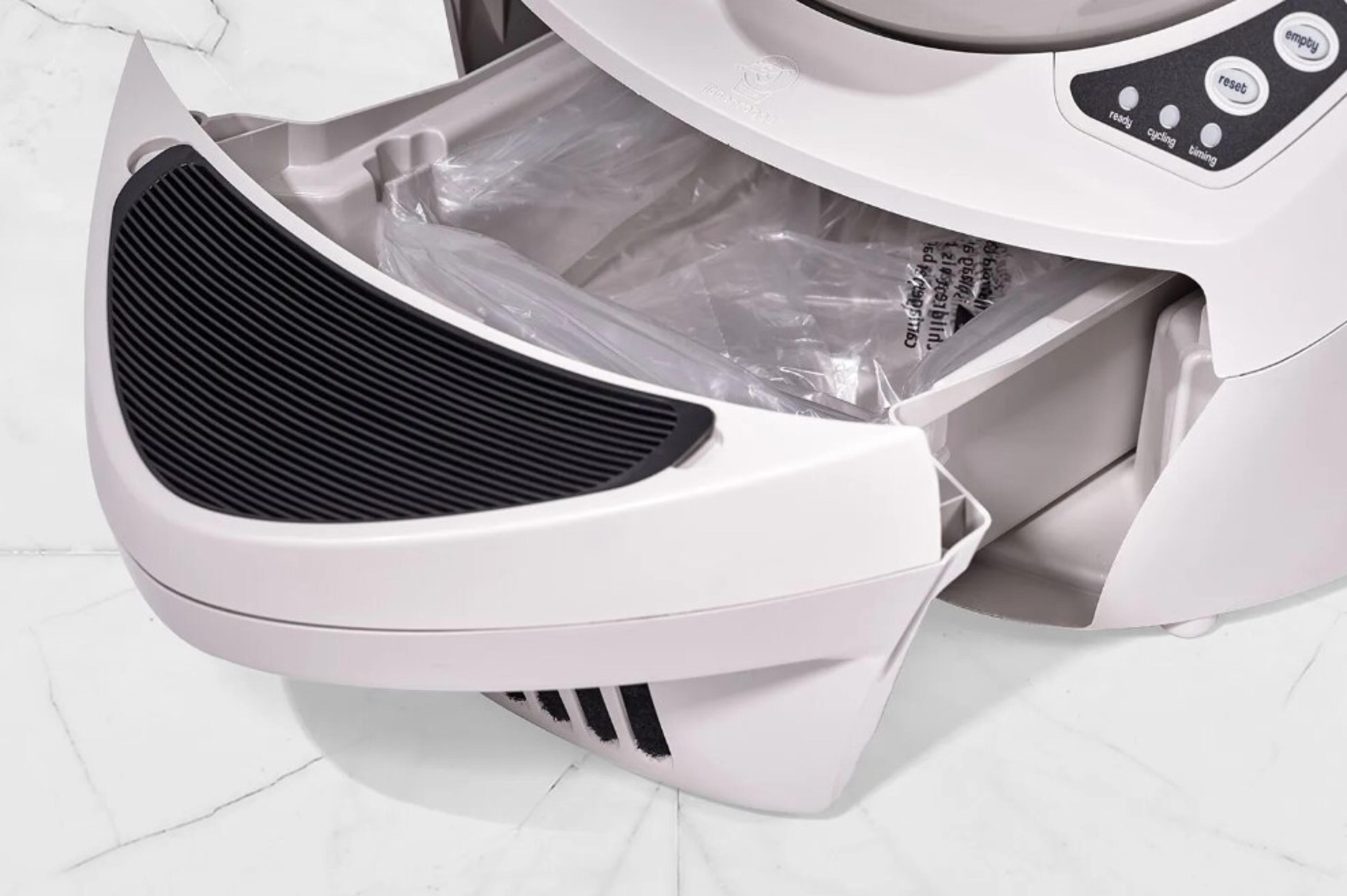 Eine weiße und schwarze Katzentoilette ist geöffnet und zeigt einen Plastikbeutel im Inneren. Knöpfe sind sichtbar.