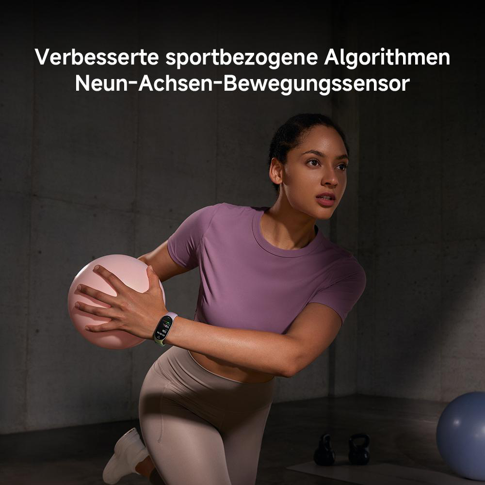 Frau in Sportkleidung mit rosa Ball und Smartwatch. Training im Fitnessstudio. Im Hintergrund befinden sich Gewichte und ein blauer Ball.