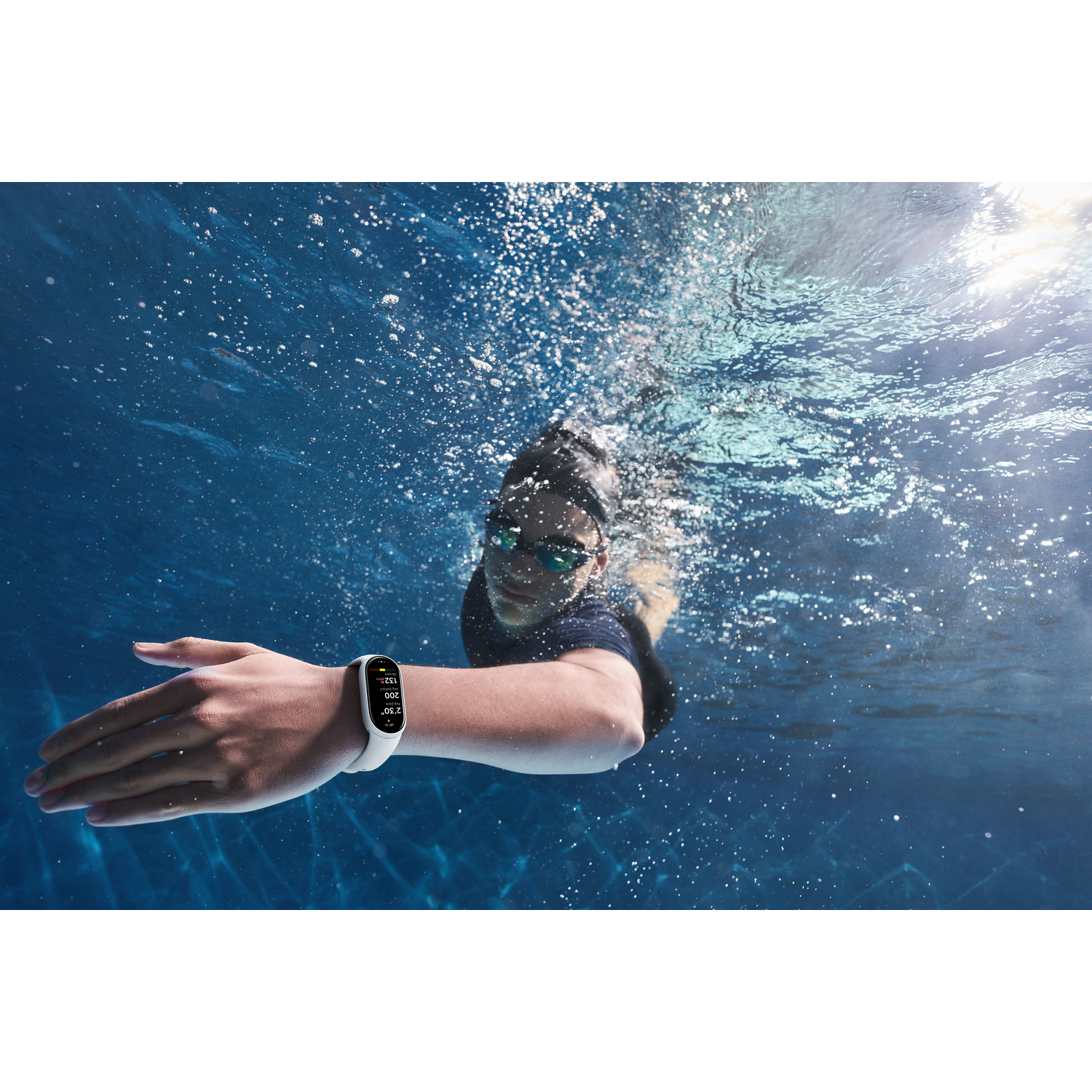 Een persoon zwemt onder water met een bril en een smartwatch. Water met bellen omringt hen. Zonlicht schijnt door het water.