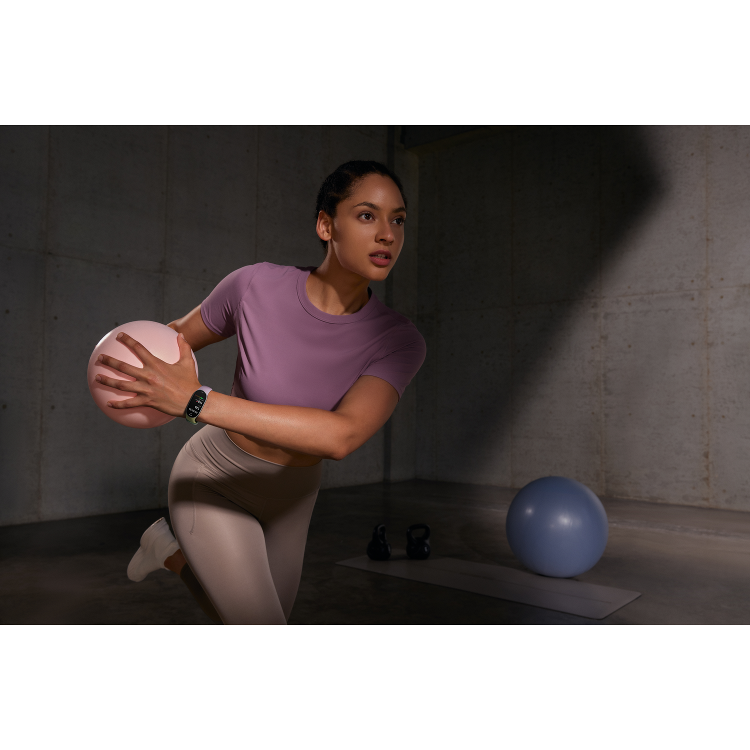 Vrouw in sportkleding met roze bal. Ze draagt ​​een smartwatch. Blauwe bal, mat en gewichten op de achtergrond.