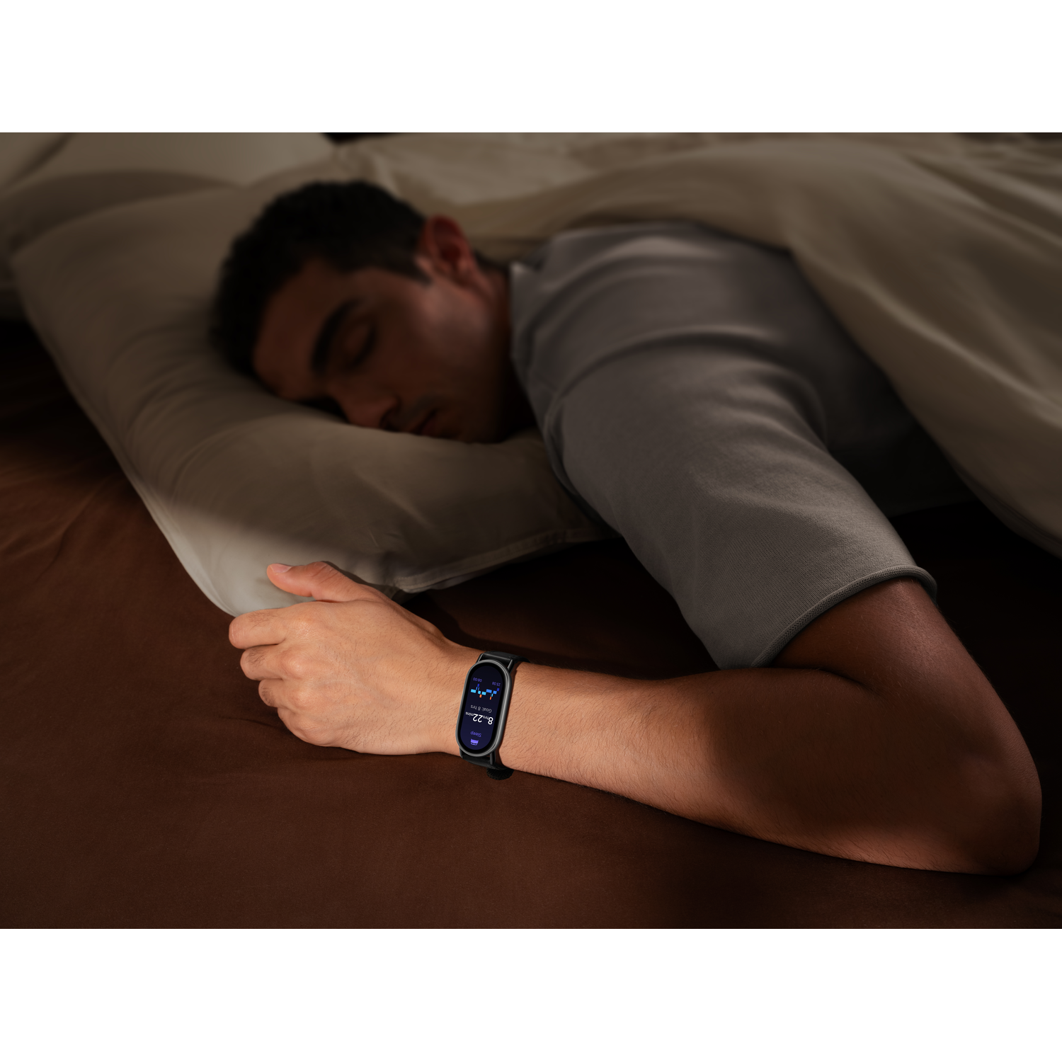 Un homme endormi au lit, portant une montre intelligente affichant des données de sommeil. L'arrière-plan montre un oreiller, un drap et un couvre-lit marron.