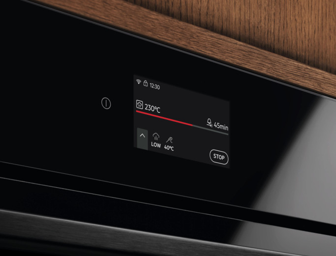 Czarny wyświetlacz piekarnika pokazujący 230°C, timer 45 min. Drewniana powierzchnia w tle. Interfejs z przyciskami i ikonami.