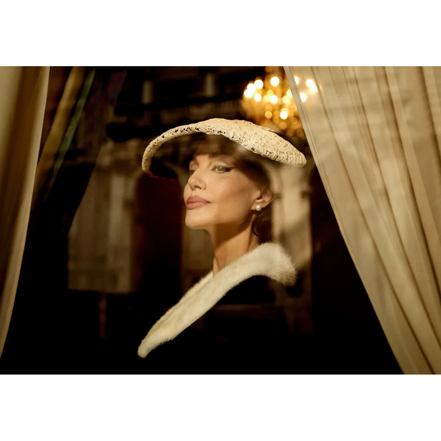 Femme avec un chapeau et un col en fourrure, vue à travers une fenêtre, avec un arrière-plan flou de lumières et de rideaux.