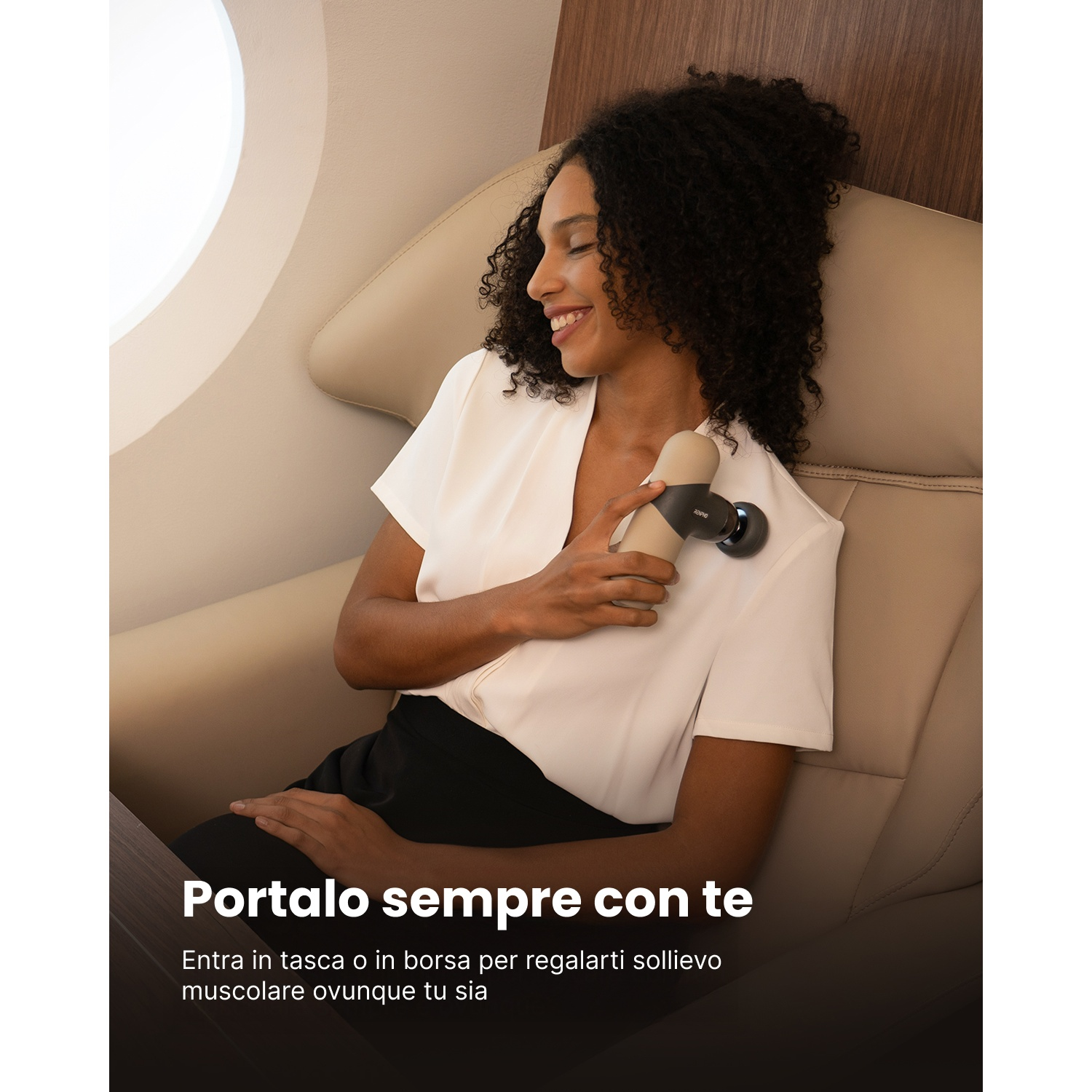Una donna sorride, tenendo in mano un dispositivo per massaggio. È seduta su una sedia beige, probabilmente in aereo. Camicia bianca e pantaloni neri.