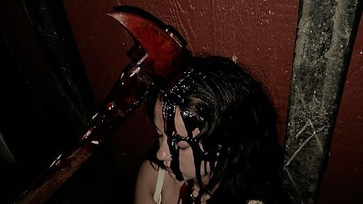 Axt in den Kopf einer Frau gesteckt, Blut tropft. Dunkle Szene, Horrorfilm. Roter Axtkopf, schwarzes Haar, weißes Oberteil.