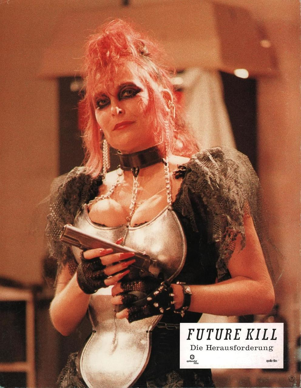 Frau mit roten Haaren und Make-up hält eine Pistole. Sie trägt ein silbernes Oberteil, einen schwarzen Halsband und Handschuhe. Das Poster sagt 'FUTURE KILL'.
