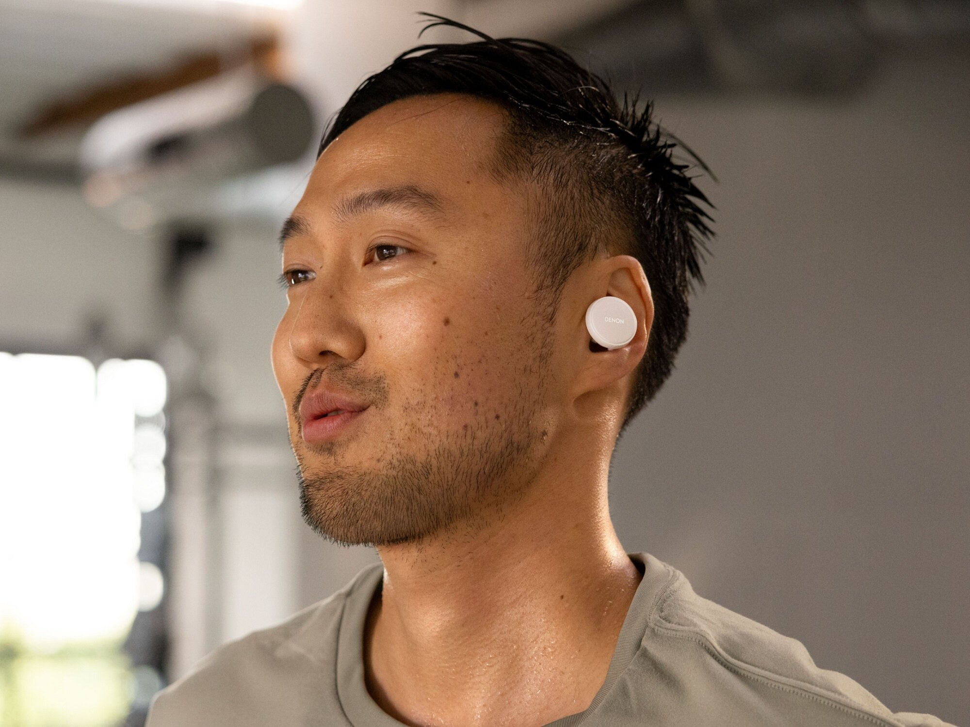 Mężczyzna z białą słuchawką w uchu. Patrzy w bok. Tło to rozmyta siłownia.