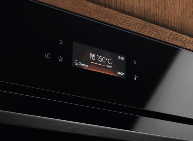 Czarny panel sterowania piekarnika z wyświetlaczem 150°C, 36min i 12:30. Drewniana powierzchnia u góry.