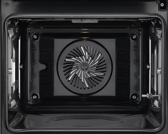 Wewnątrz czarnego piekarnika widoczny jest wentylator. Wnętrze piekarnika jest ciemne, z okrągłym wentylatorem pośrodku.