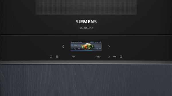Un horno microondas Siemens negro con una pantalla digital que muestra verduras frescas. El horno tiene varios botones y un panel de madera.