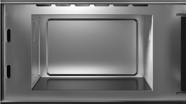 Interior de un microondas metálico. El interior es rectangular. La puerta está cerrada. La escena está bien iluminada, con un aspecto brillante.