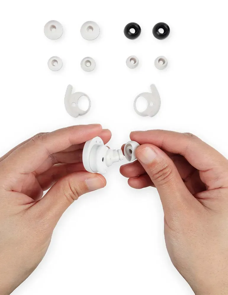 Ręce składające słuchawki. Wyświetlane są różne końcówki słuchawek. Widoczne są białe i czarne końcówki, osoba trzyma białe części.