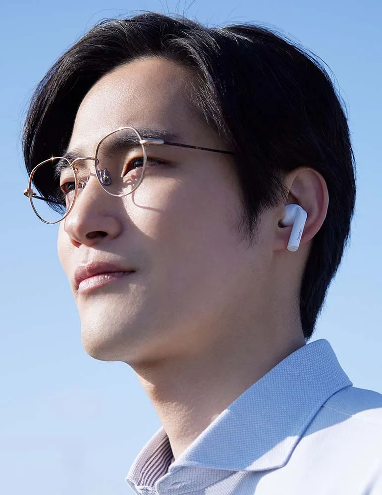 Mężczyzna w okularach i słuchawkach patrzy w czyste niebo. Ma na sobie jasnoniebieską koszulę. Tło jest błękitne.